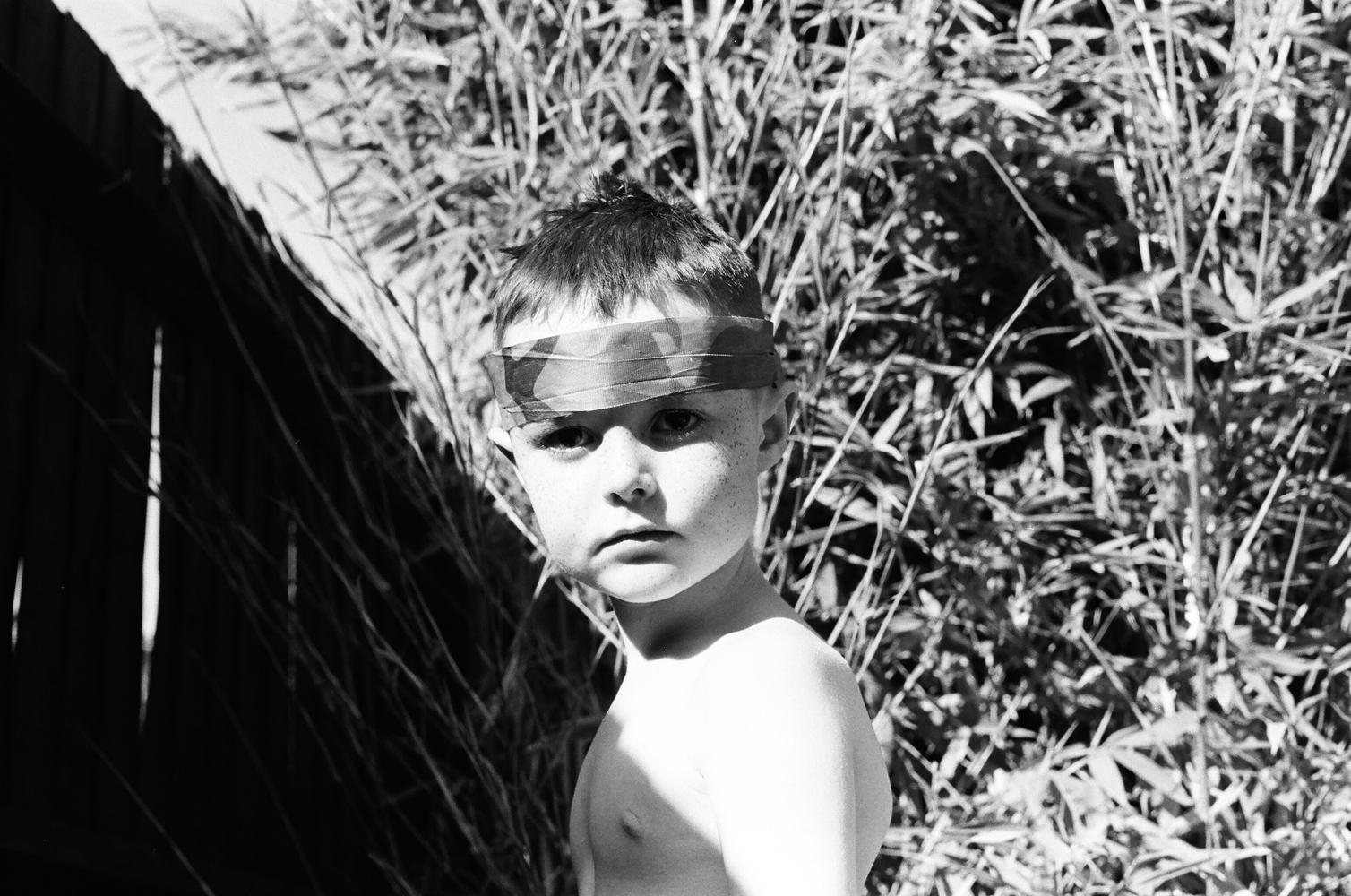 A black and white film photograph of a young boy in the garden