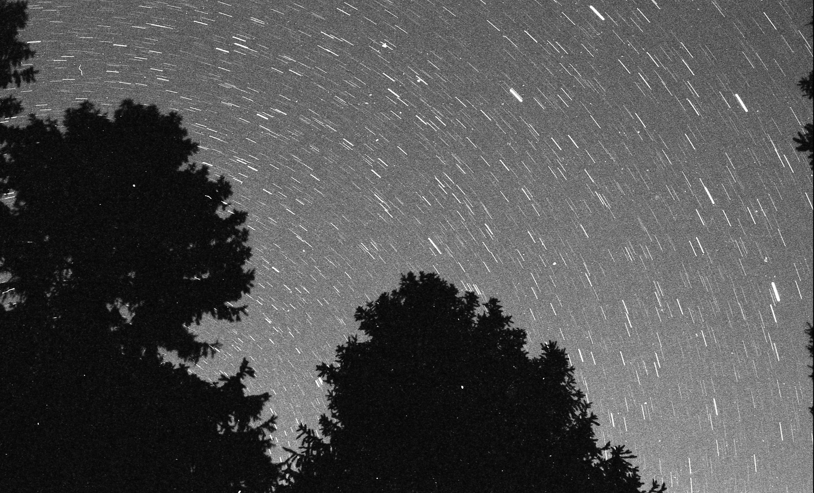 Photograph tracking the movement of the stars as the earth rotates, leaving trails where the stars once were. Black and white,